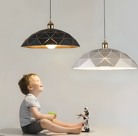 Two geometric pendant lights with black and white shades, featuring gold accents, hanging above a young boy holding a toy and looking up at the lights, with a small robot toy beside him.