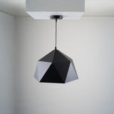 A geometric black pendant light with a faceted, polygonal design is suspended from a white ceiling. The fixture is fixed directly to a square ceiling mount.
