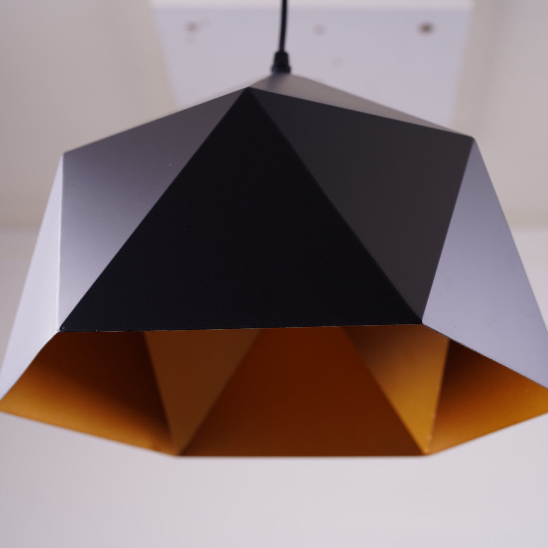 A geometric black pendant light with a faceted design and a gold interior is fixed to a white ceiling.