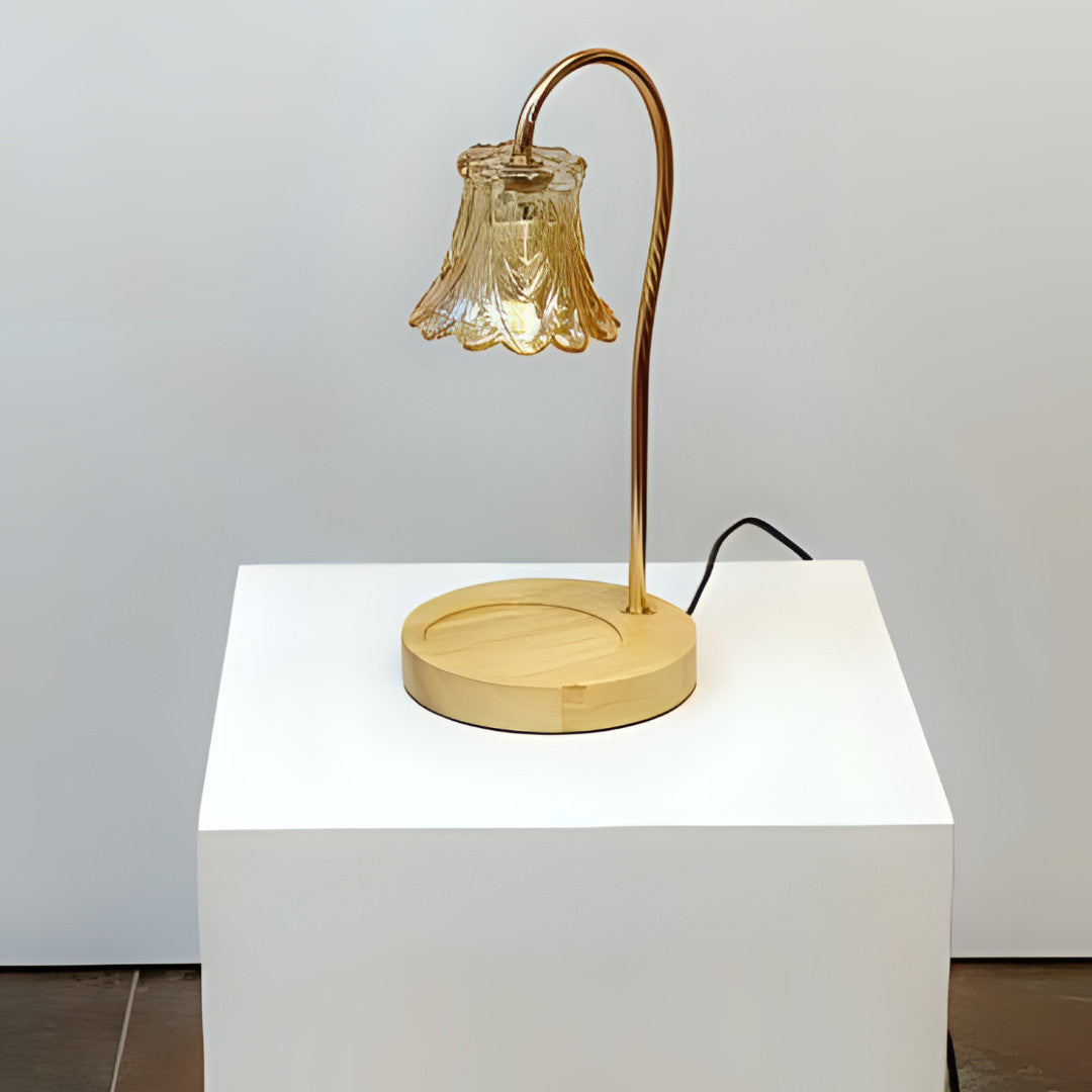 A vintage-inspired table lamp with a curved bronze arm holding a delicate bell-shaped glass shade, sitting on a round wooden base. Placed on a round white table.