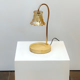 A vintage-inspired table lamp with a curved bronze arm holding a delicate bell-shaped glass shade, sitting on a round wooden base. Placed on a round white table.