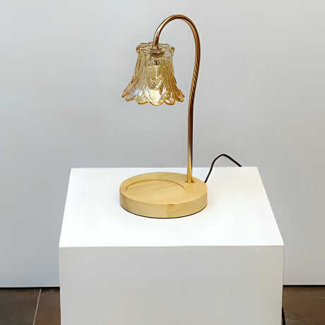 A vintage-inspired table lamp with a curved bronze arm holding a delicate bell-shaped glass shade, sitting on a round wooden base. Placed on a round white table.