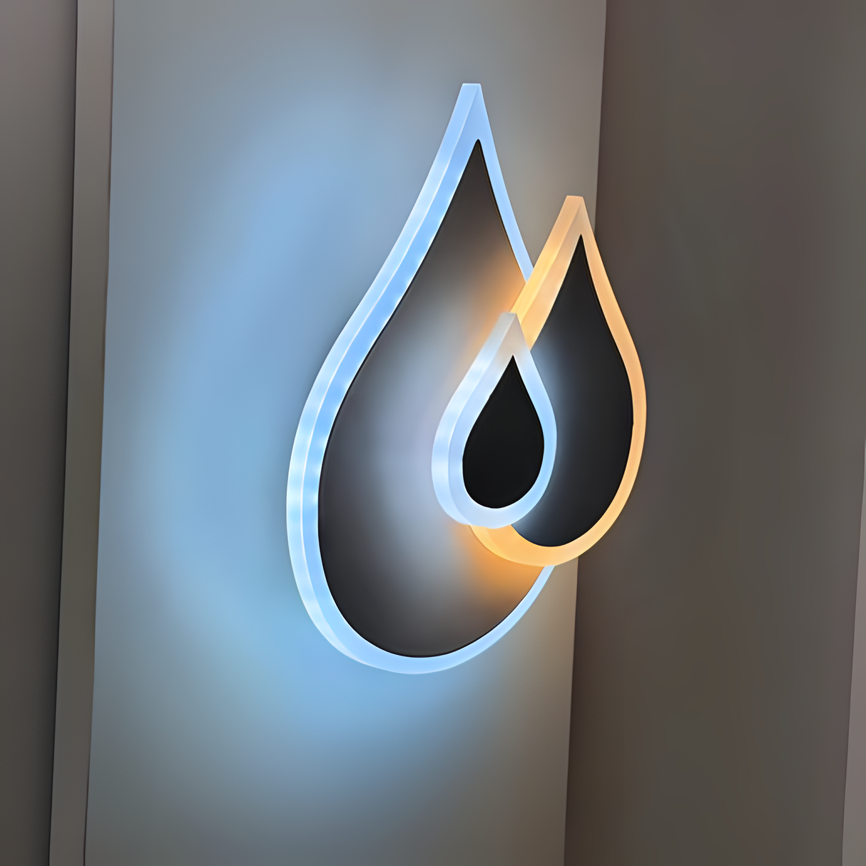Wall-mounted LED light fixture shaped like two overlapping water droplets, with a soft white and warm white glow illuminating the surrounding wall.