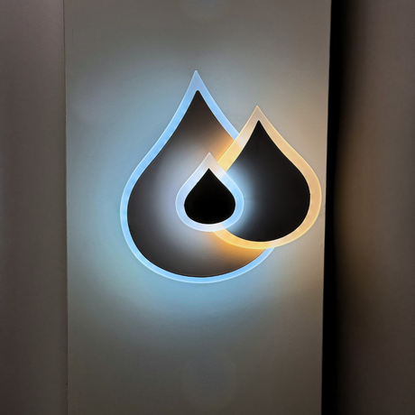 Wall-mounted LED light fixture shaped like two overlapping water droplets, with a soft white and warm white glow illuminating the surrounding wall.