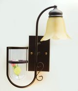 A rustic-inspired wall light with a brown metal  frame, a curved arm, and a frosted glass shade in a flower-like shape . Below it, a small decorative glass shelf holds a flower.
