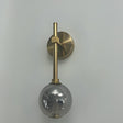 A wall-mounted gold fixture with a grey glass globe hanging from a slim vertical rod.