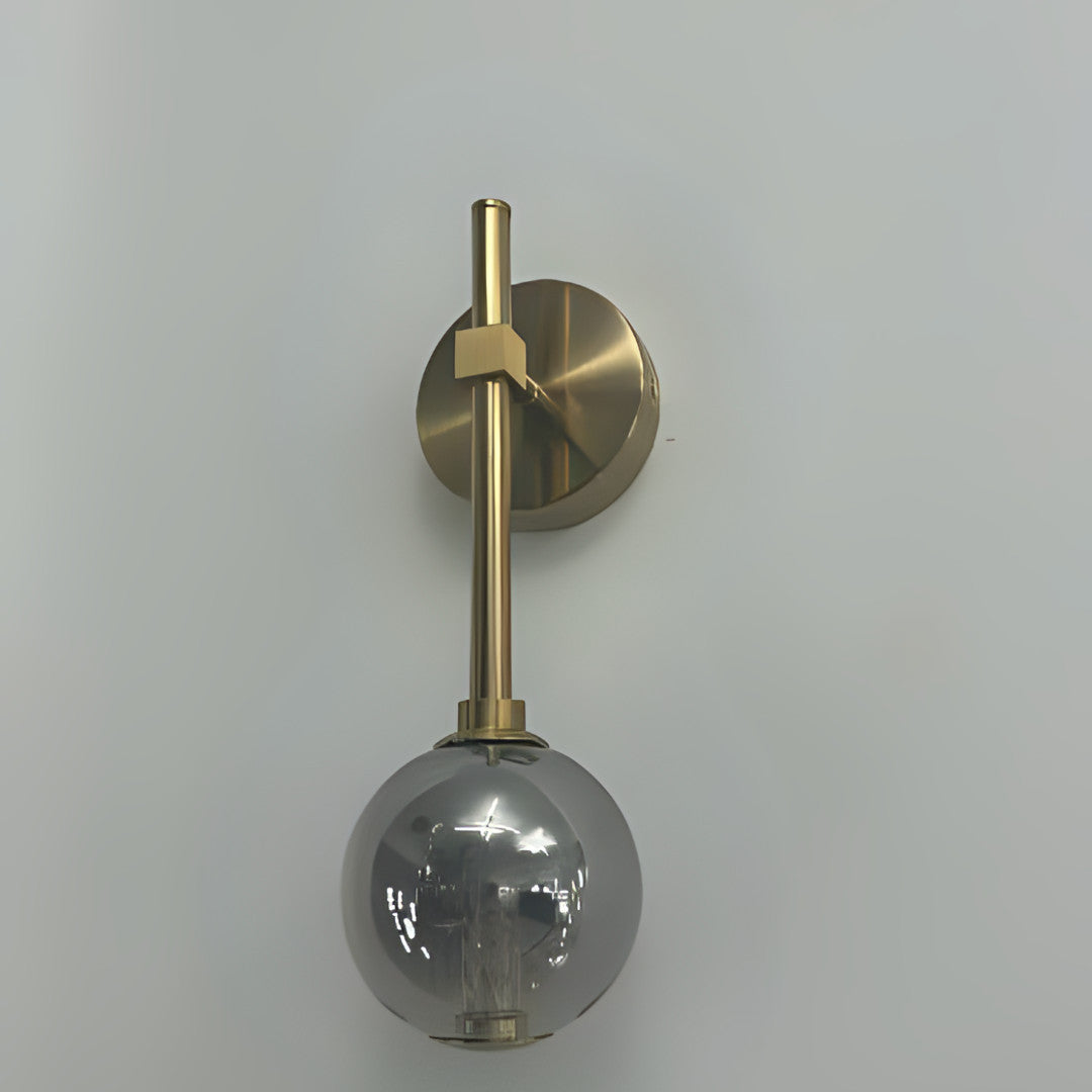 A wall-mounted gold fixture with a grey glass globe hanging from a slim vertical rod.
