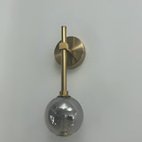 A wall-mounted gold fixture with a grey glass globe hanging from a slim vertical rod.