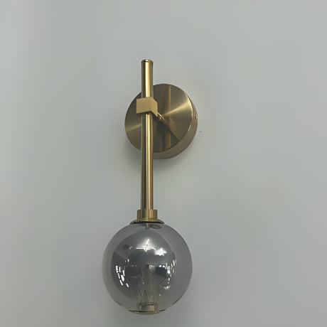 A wall-mounted gold fixture with a grey glass globe hanging from a slim vertical rod.