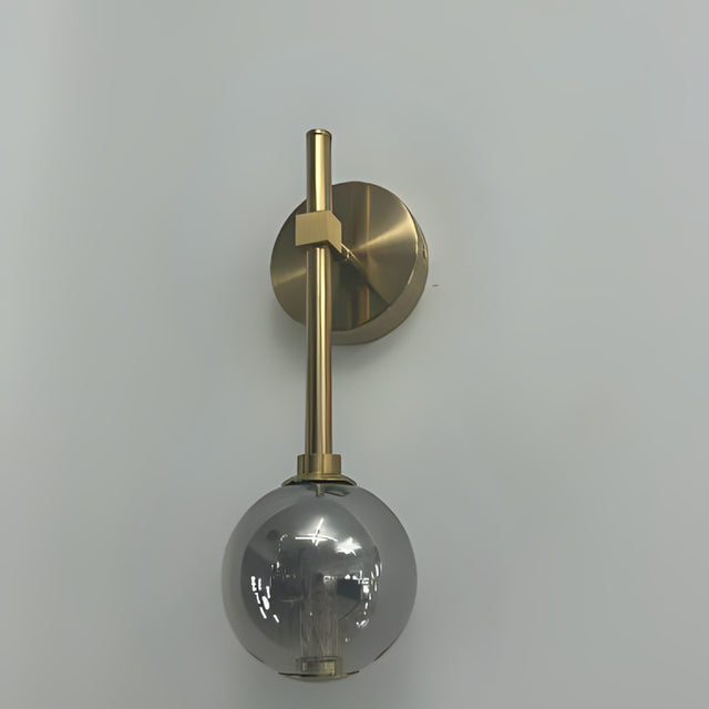 A wall-mounted gold fixture with a grey glass globe hanging from a slim vertical rod.