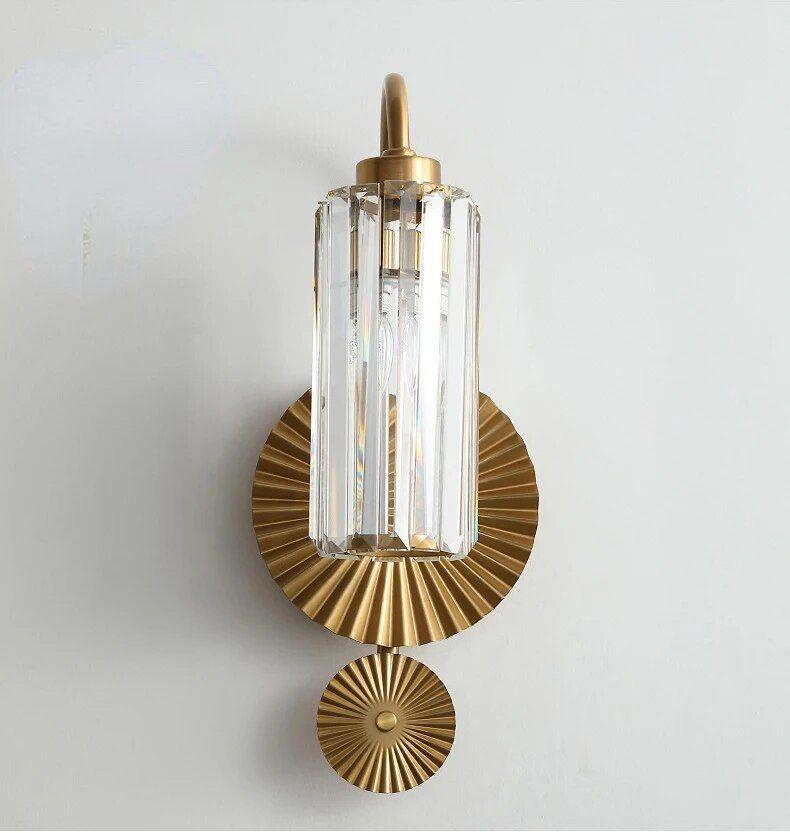 A modern brass wall light with a vertically ribbed glass shade and a circular decorative backplate.