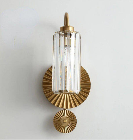 A modern brass wall light with a vertically ribbed glass shade and a circular decorative backplate.